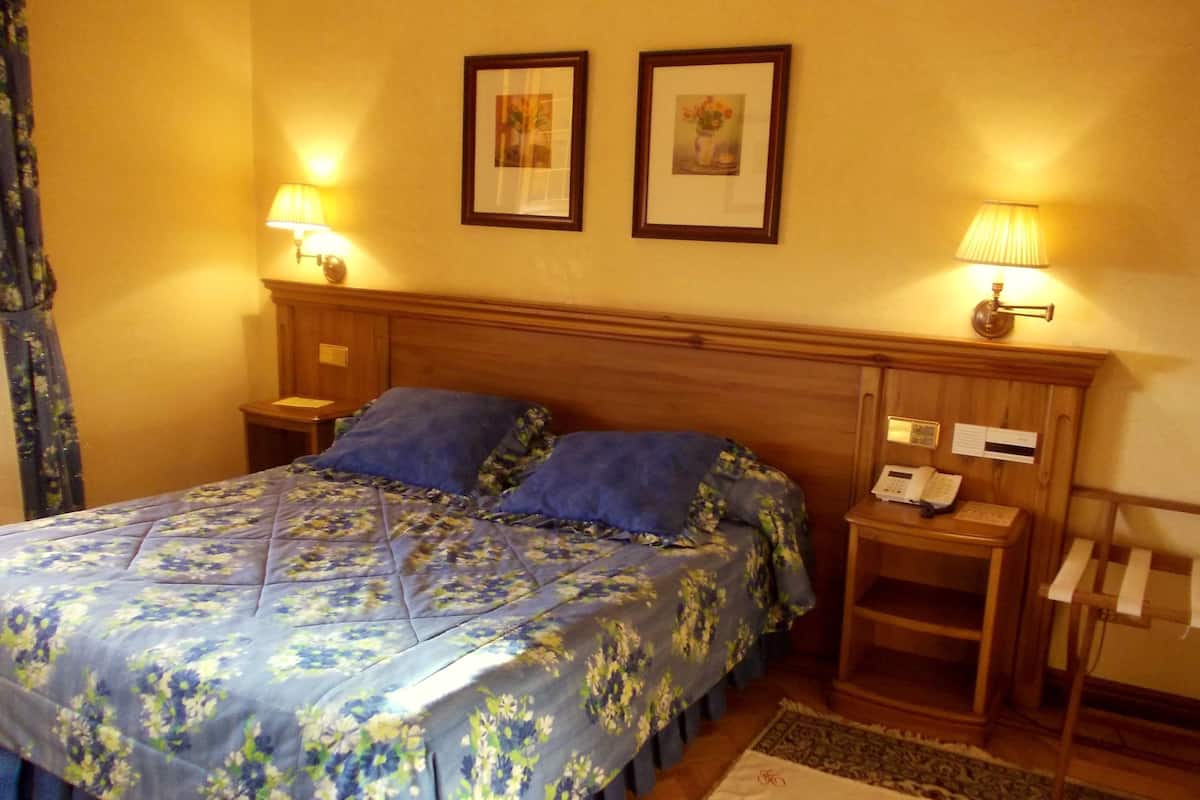 Ein Hotelzimmer mit einem Bett, zwei Nachttischlampen, einem Nachttisch mit Telefon und einem gerahmten Bild an der Wand.