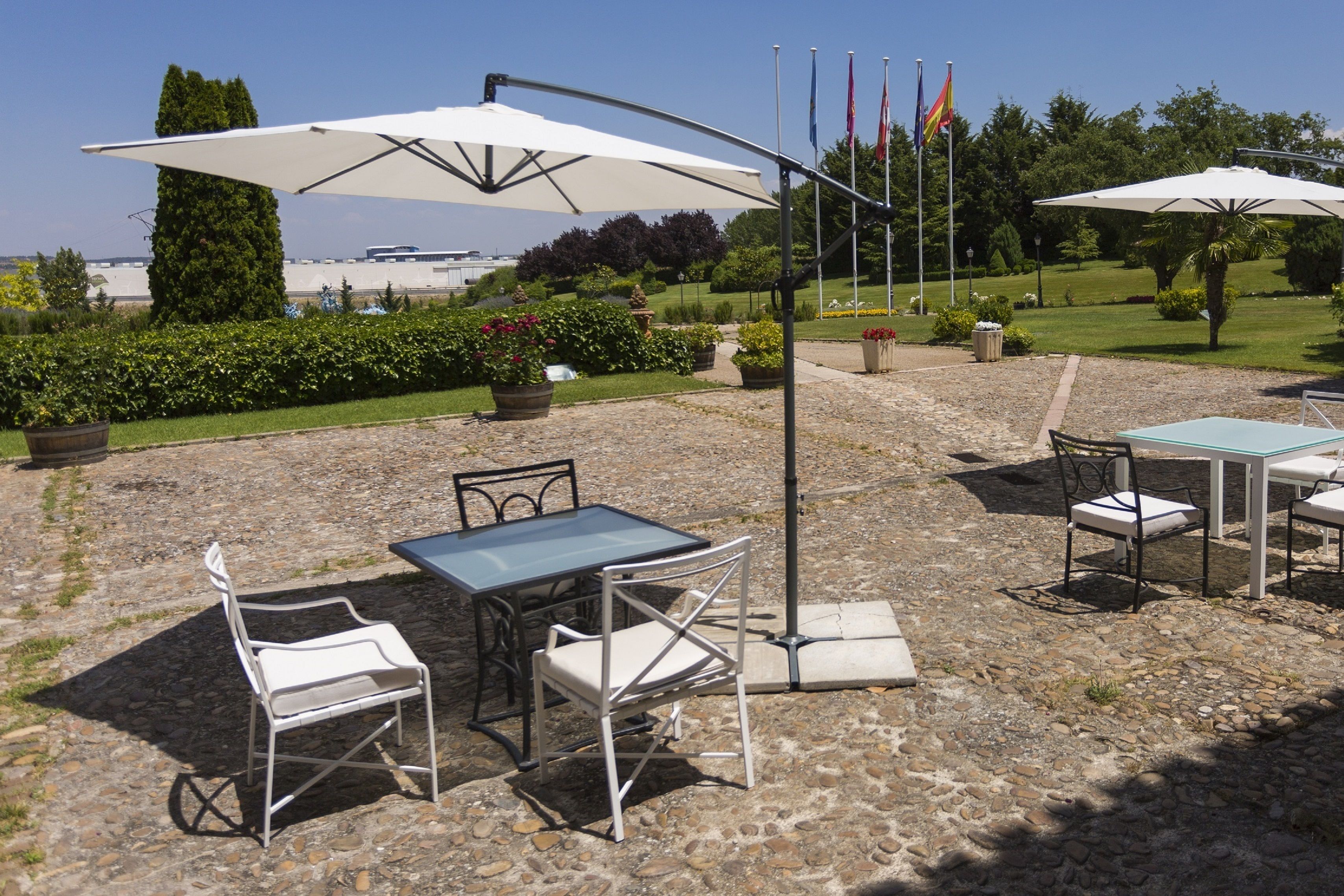 An outdoor patio with stone flooring, metal tables and chairs, and white umbrellas.