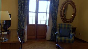 Un salón con un escritorio de madera, una silla, un sillón azul, un espejo redondo y una araña.