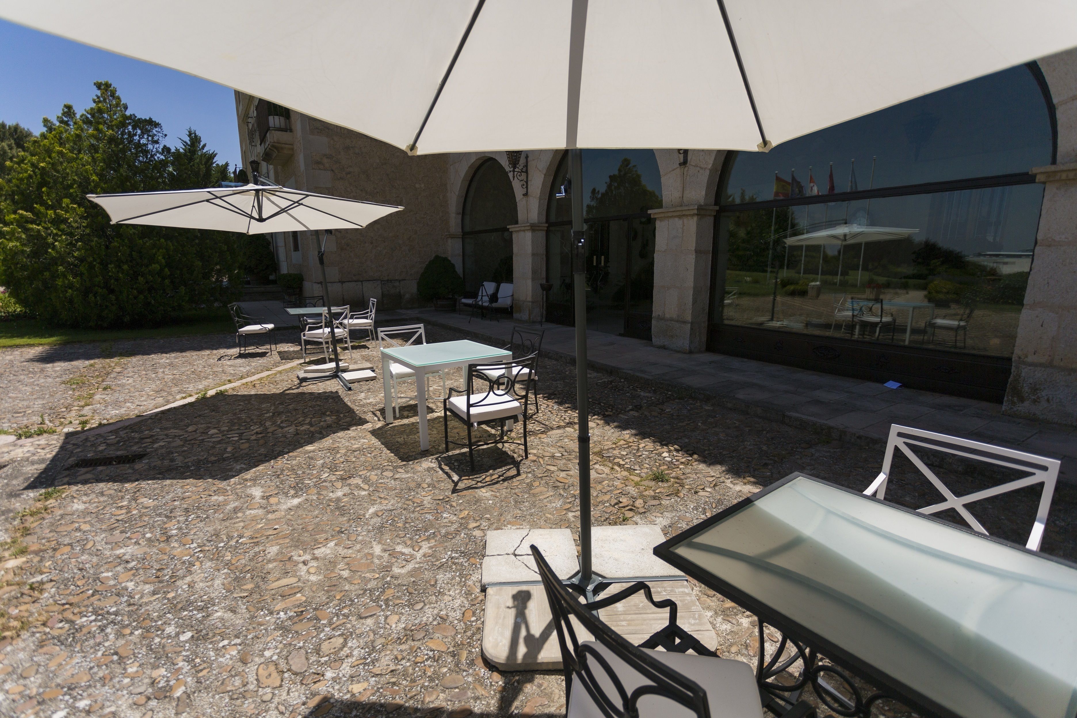 Ein Außenbereich mit Terrasse, Steinboden, Tischen, Stühlen und Sonnenschirmen.