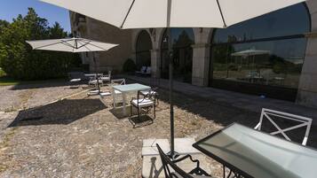 Ein Außenbereich mit Terrasse, Steinboden, Tischen, Stühlen und Sonnenschirmen.