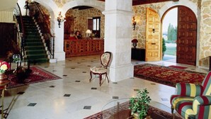 A spacious lobby with a grand staircase, stone walls, and a wooden ceiling.