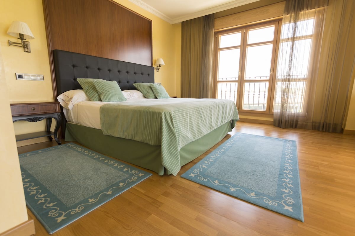 Ein Hotelzimmer mit einem großen Bett, zwei Nachttischen, einem Fenster mit Vorhängen und Holzboden.