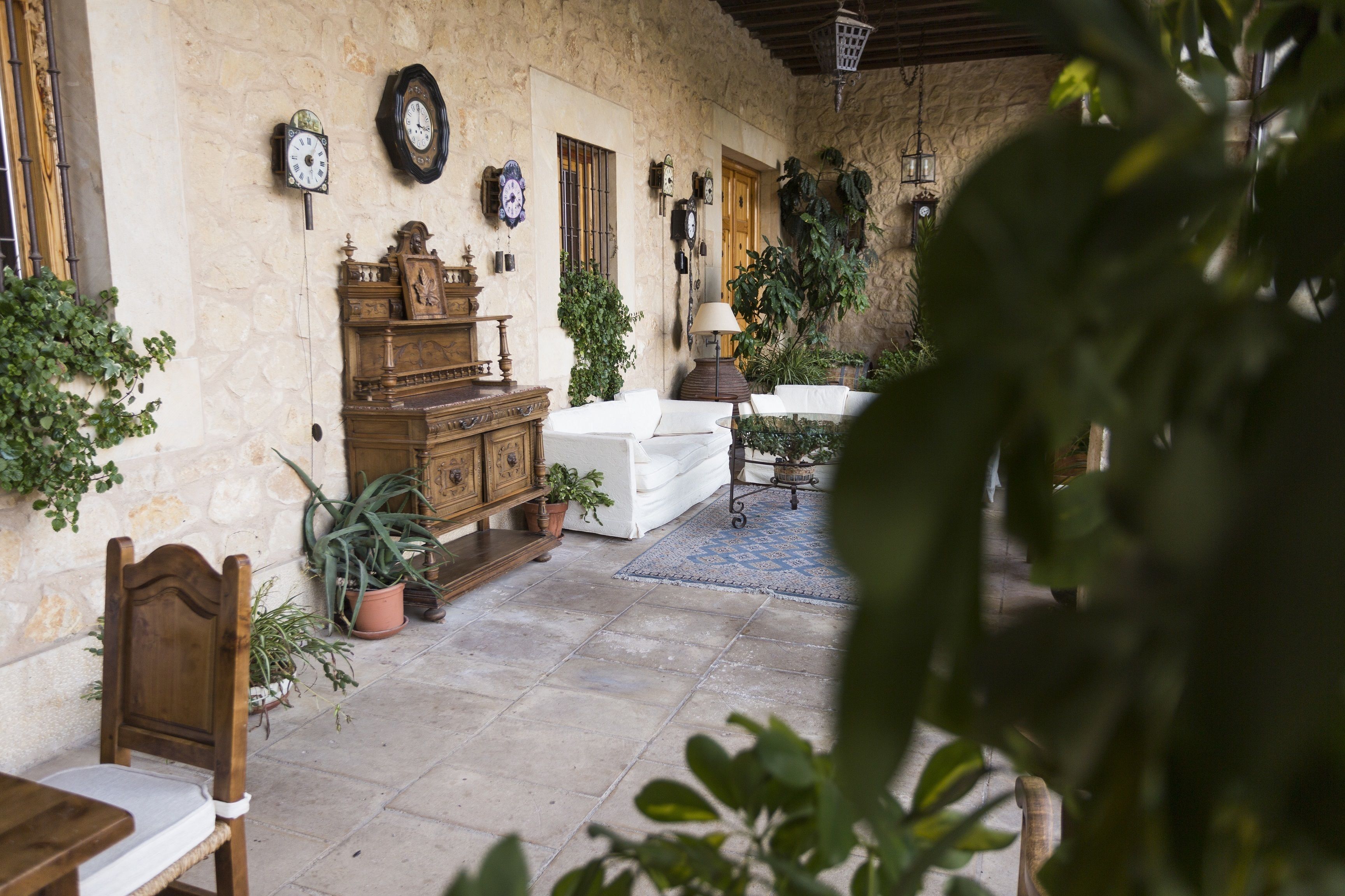A cozy patio with stone walls, a wooden cabinet, a white sofa, and potted plants.