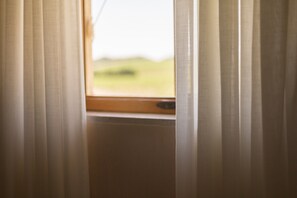A window with sheer curtains, a wooden frame, and a view of a green landscape.
