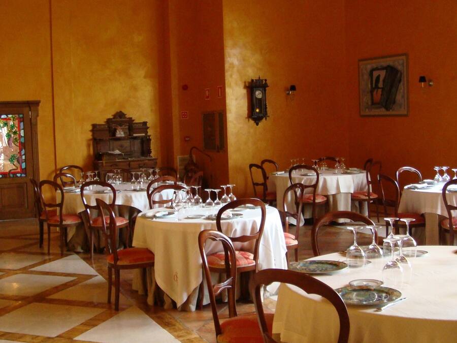 A dining area with multiple round tables set for service, chairs, and a large wooden piano in the background.