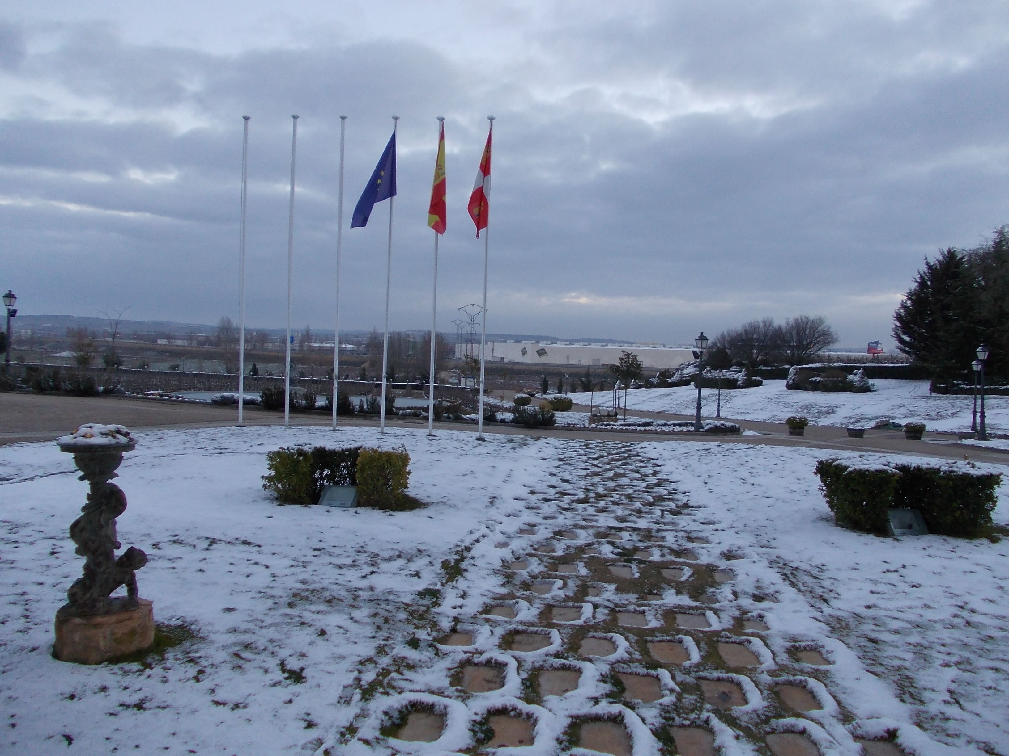 A snow-covered pathway leading to a building with multiple flags.