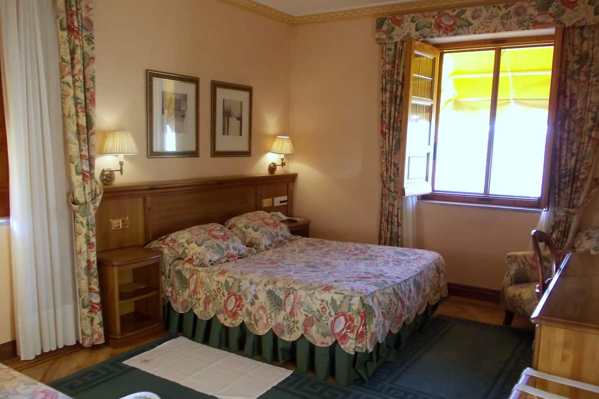 Ein Schlafzimmer mit einem Bett, zwei Nachttischen, einem Sessel, einem Fenster mit Vorhängen und einer Heizung.