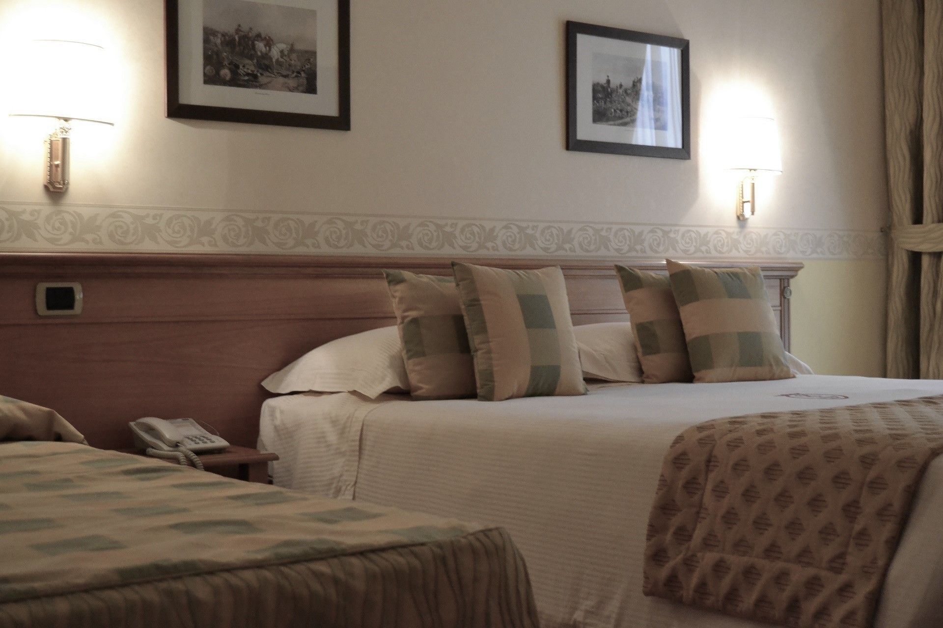 Een hotelkamer met twee bedden, een nachtkastje met een telefoon en twee wandlampen.