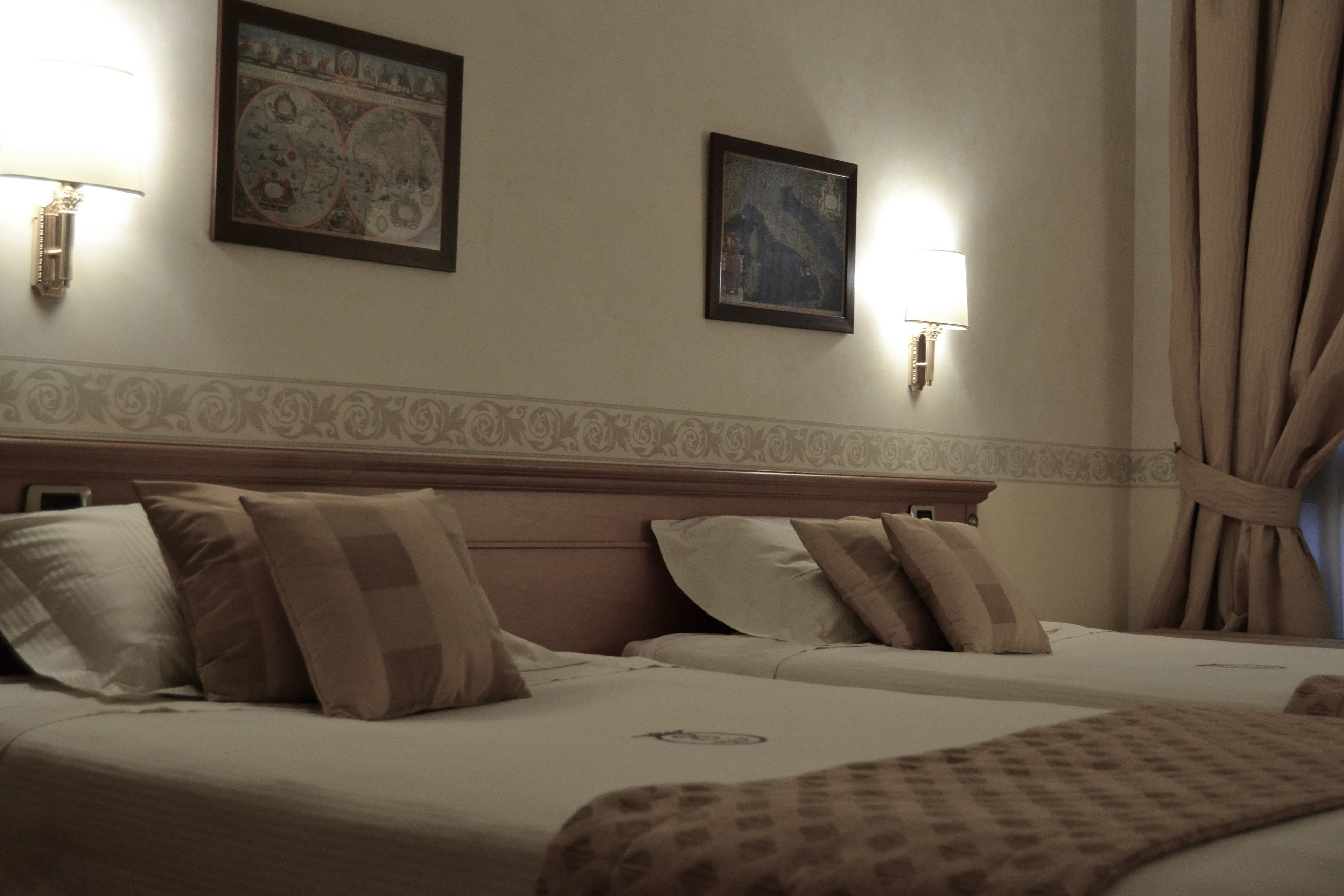 Een hotelkamer met twee bedden, een hoofdbord met decoratief paneel, wandlampen en ingekaderde kunstwerken.