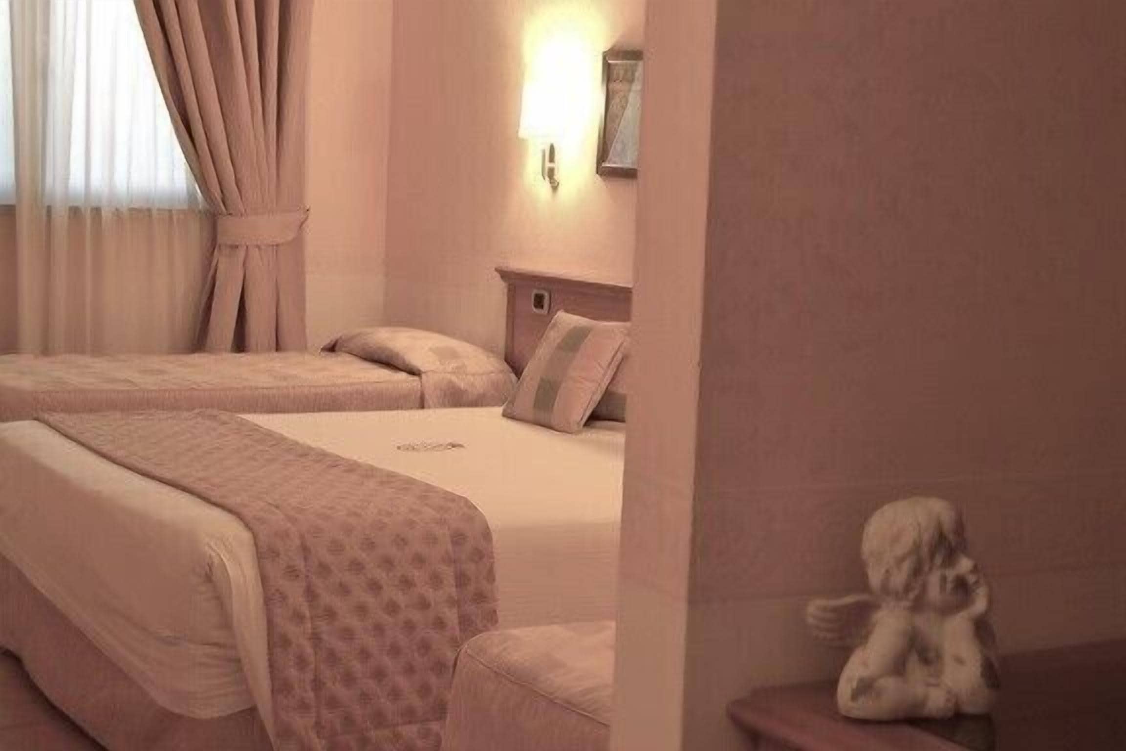 A hotel room with two beds, a nightstand, a wall-mounted light, and a statue.