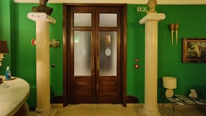 A room with a green wall, a wooden door with glass panels, and classical sculptures on columns. - Hotel Seccy Boutique Art & Museum (Fiumicino)