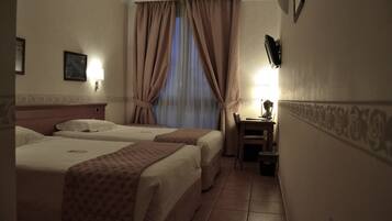 Quarto de hotel com duas camas, uma mesinha com uma luminária, uma cadeira e uma janela com cortinas.