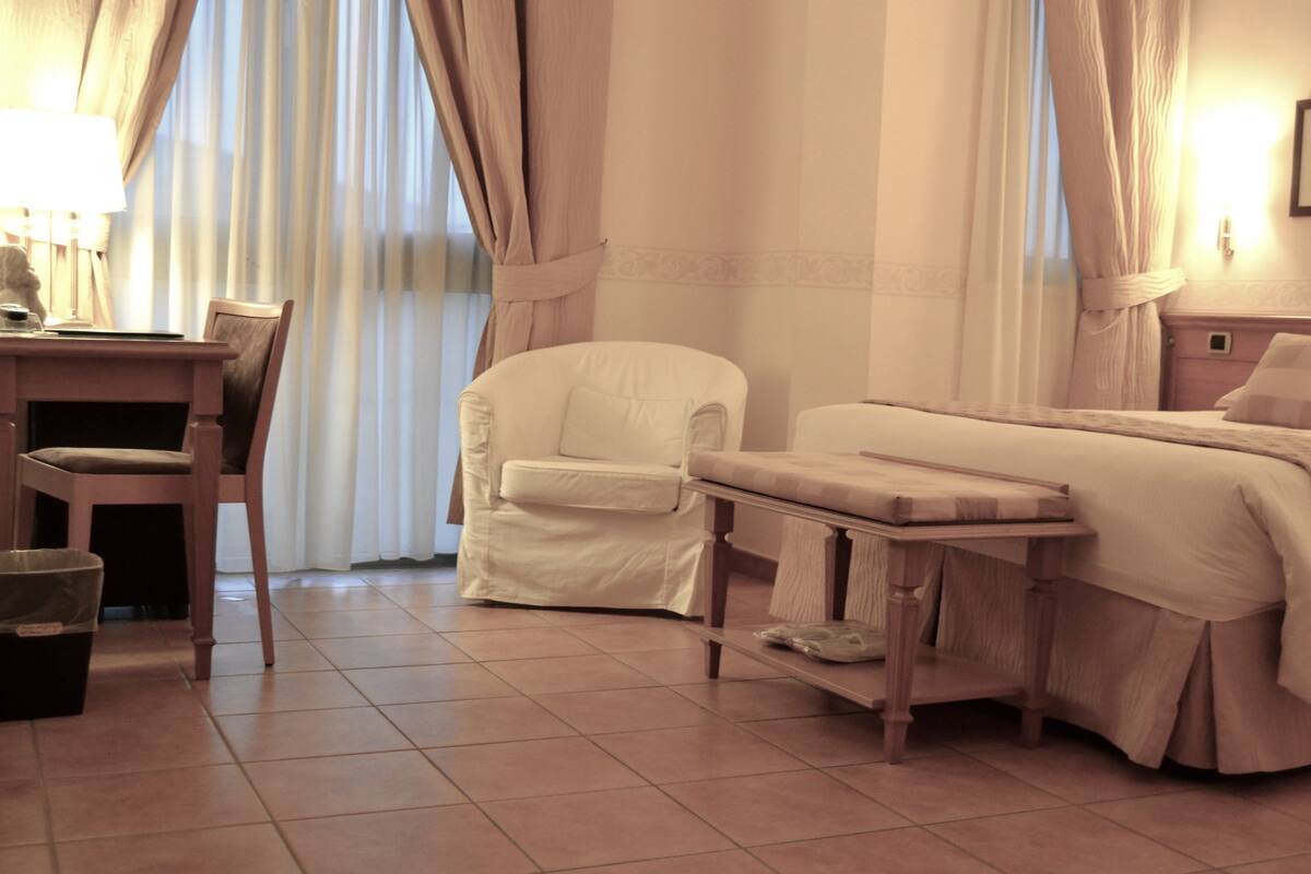 A hotel room with a bed, a chair, a desk, and a lamp.