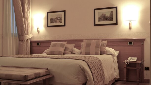 A neatly arranged bedroom with a large bed, bedside tables, a bedside lamp, and framed pictures on the wall. - Hotel Seccy Boutique Art & Museum (Fiumicino)