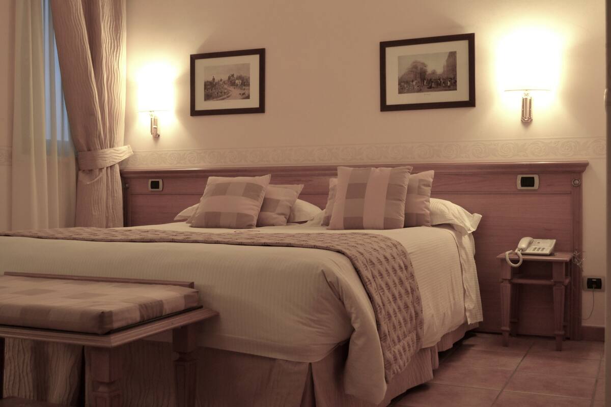 A neatly arranged bedroom with a large bed, bedside tables, a bedside lamp, and framed pictures on the wall.