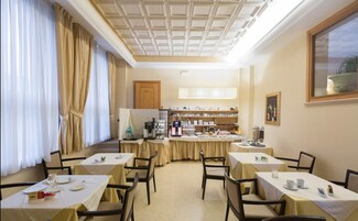 Uma sala de jantar com mesas preparadas para o café da manhã, um espaço para café e um buffet com diversos pratos.