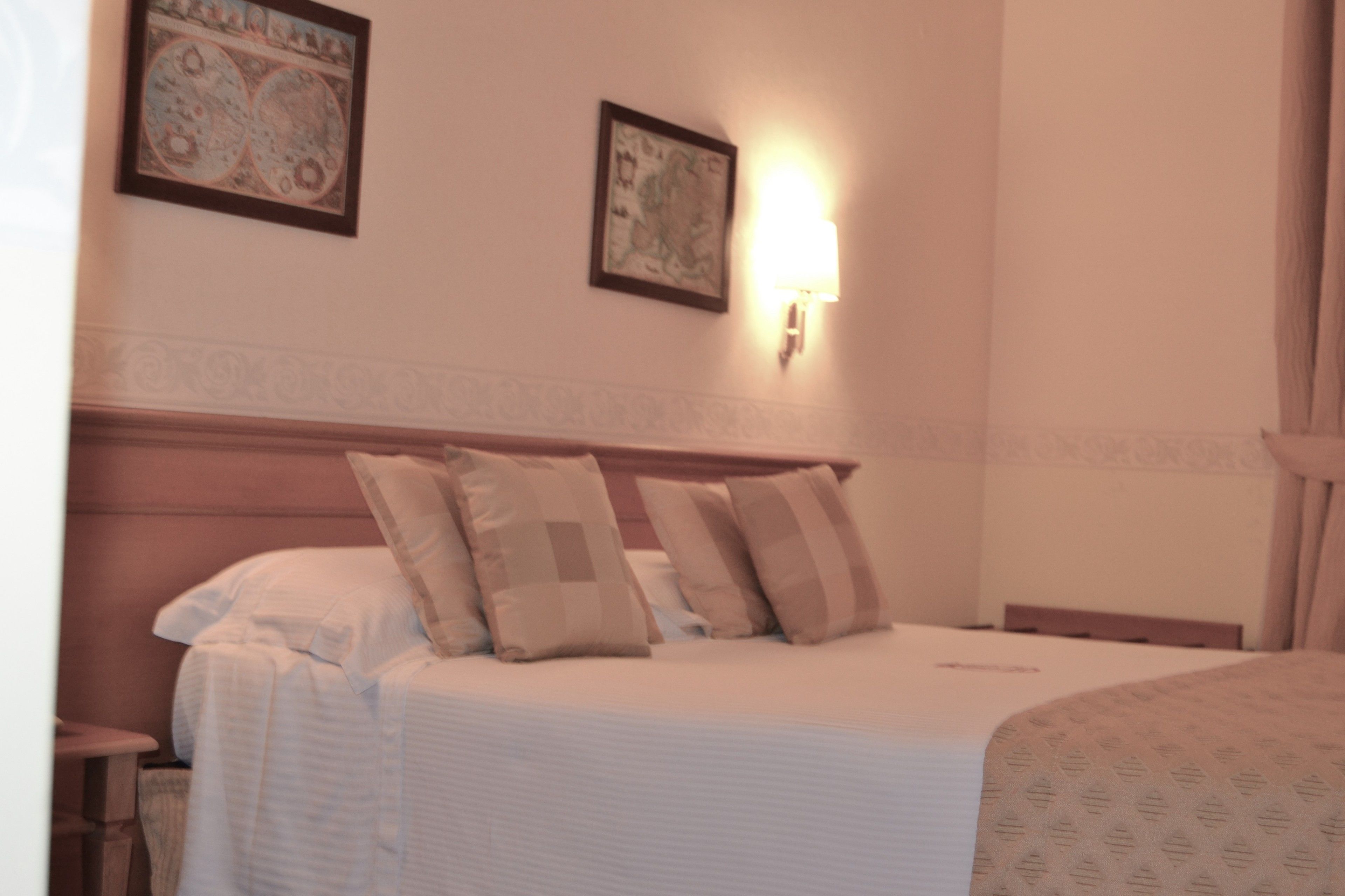 Una camera d'albergo con un letto rifatto, due quadri appesi al muro e un comodino con una lampada.