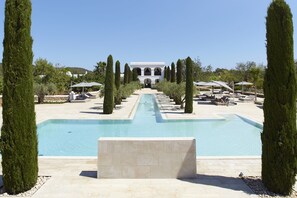 A pool area with a central pool, surrounded by tall cypress trees and lounge chairs.