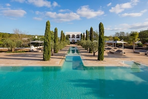 A pool area with a clear view of a building in the background, surrounded by trees and sun loungers.
