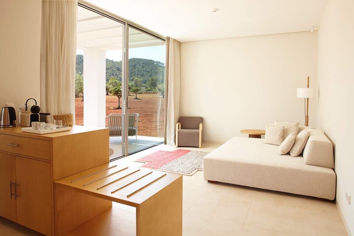 A modern hotel room with a wooden desk, a sofa, and a view of a red landscape through large glass doors.