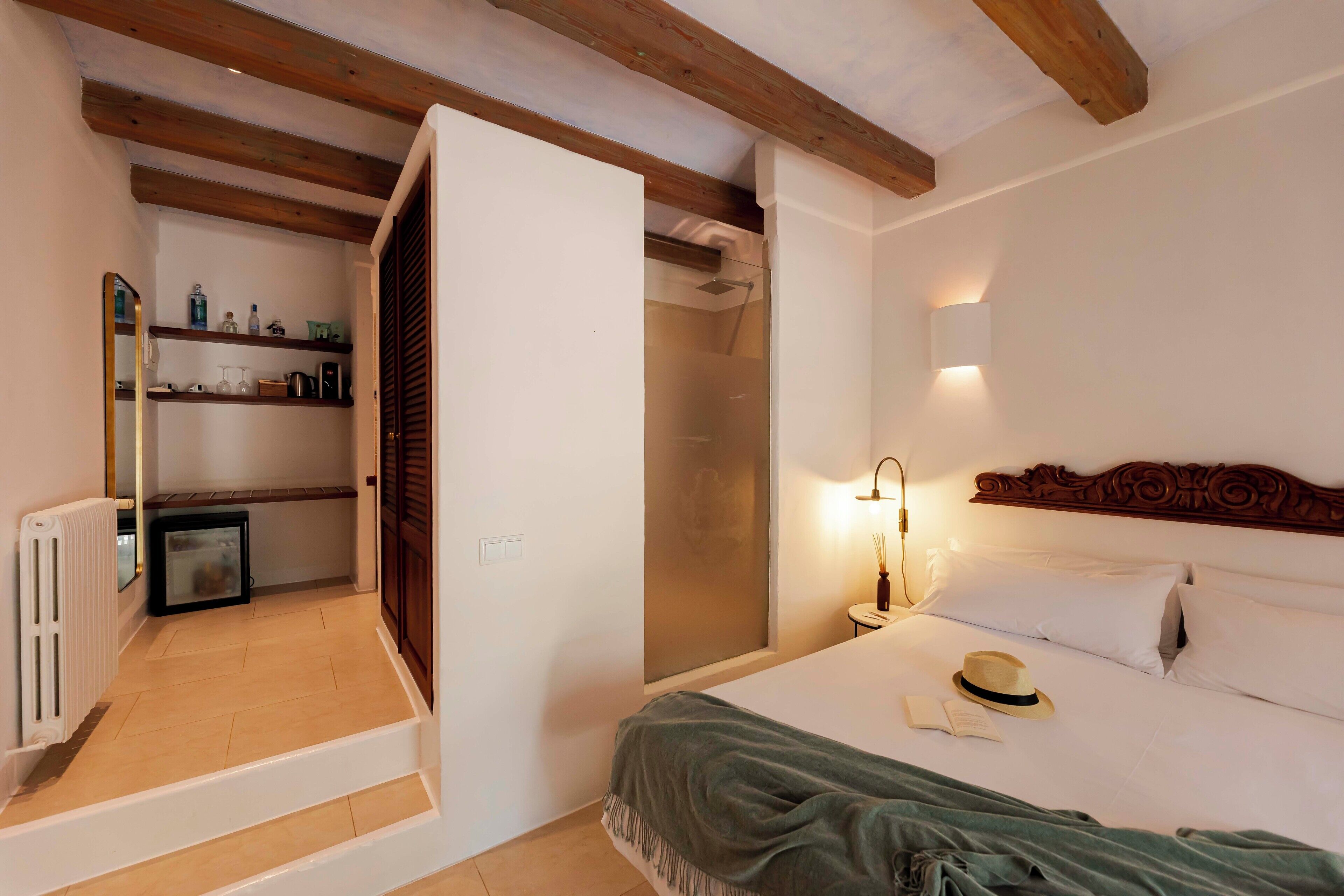 A hotel room with a bed, a bedside lamp, a hat, and a small table.