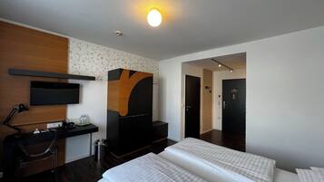 A hotel room with a bed, a desk with a computer, a TV, a wardrobe, and a door leading to another room.