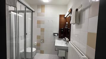 Un baño moderno con cabina de ducha de vidrio, inodoro blanco, lavamanos con espejo y un radiador.
