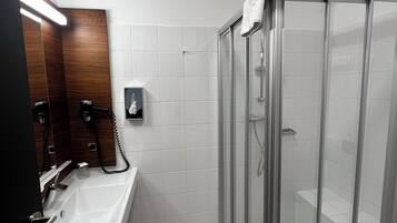Un baño moderno con cabina de ducha de vidrio, un lavamanos con espejo y un perchero para toallas.
