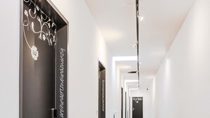 A hallway with black doors, each with a decorative pattern and text. The hallway has a green carpet and white walls. - H+ Hotel Ried (Ried im Innkreis)