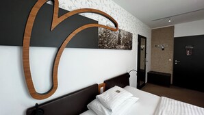 A hotel room with a large bed, a wooden headboard, a wall-mounted artwork, and a door with a mirror. - H+ Hotel Ried (Ried im Innkreis)