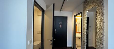 Un pasillo moderno con suelo de madera, una puerta negra con pantalla digital y una pared texturizada a la derecha.