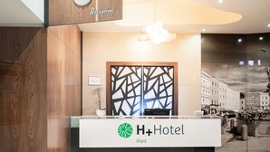 A reception desk with a clock and a sign for H+Hotel in Riegersberg. - H+ Hotel Ried (Ried im Innkreis)