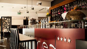 A modern bar area with a red and black color scheme, featuring a bar counter, multiple hanging pendant lights, and a ceiling with a perforated design.