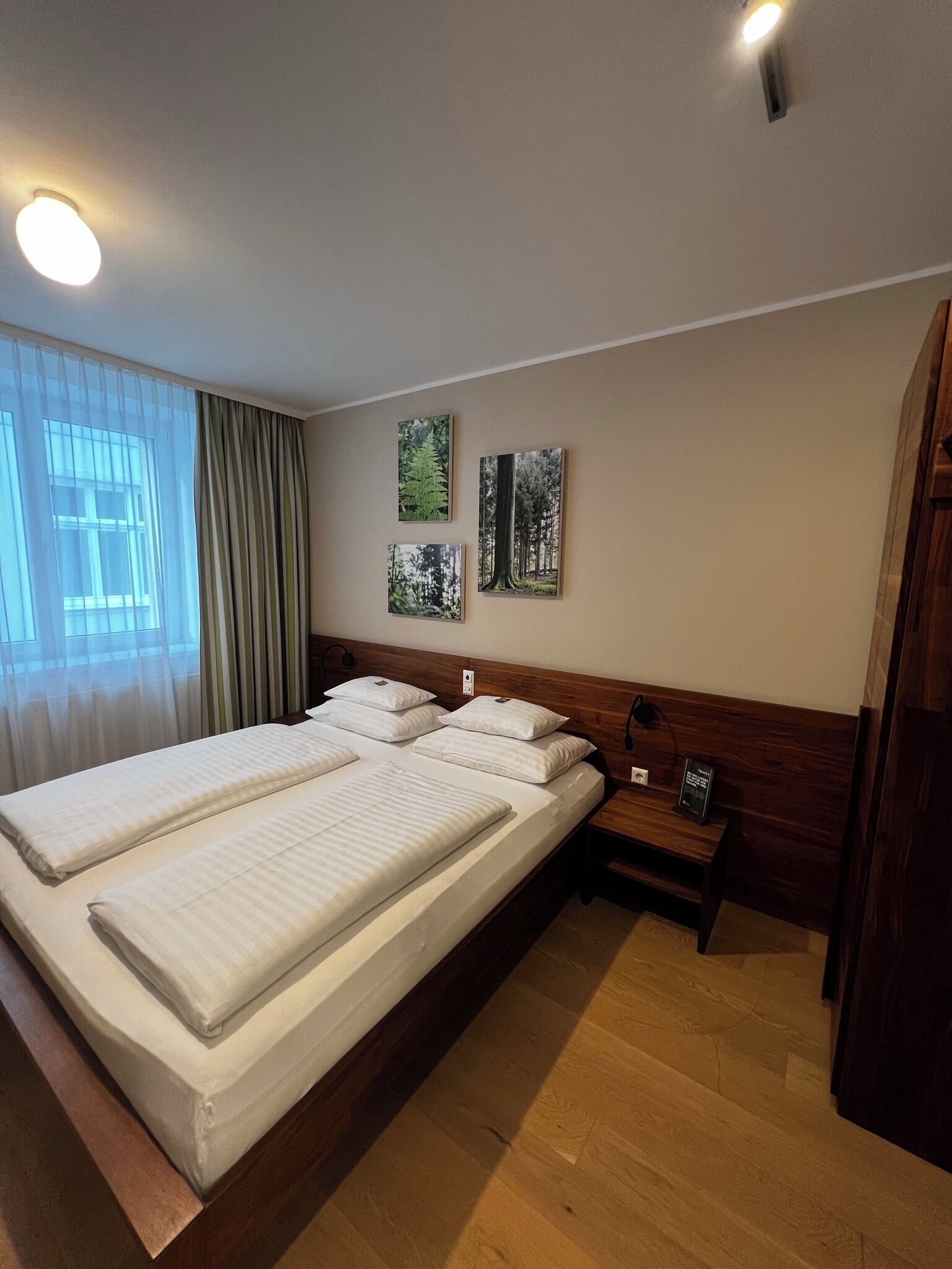 Quarto de hotel com cama de casal, mesa de cabeceira e janela com cortinas.