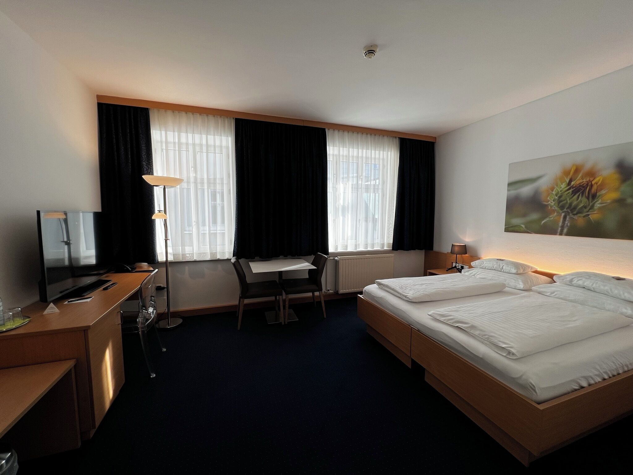 Een hotelkamer met een bed, bureau, stoel en een groot raam met gordijnen.