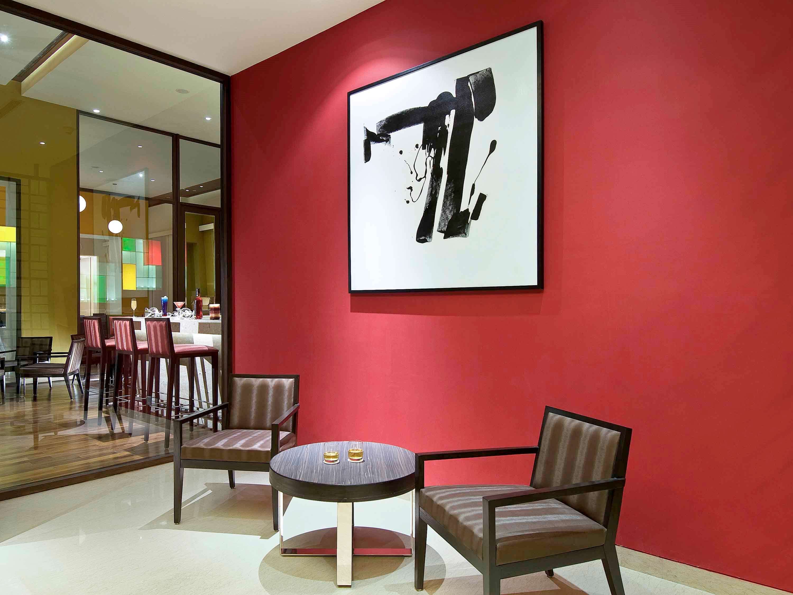 Un interior moderno con una pared de acento roja, una mesa redonda con dos sillas y un cuadro abstracto de gran tamaño.
