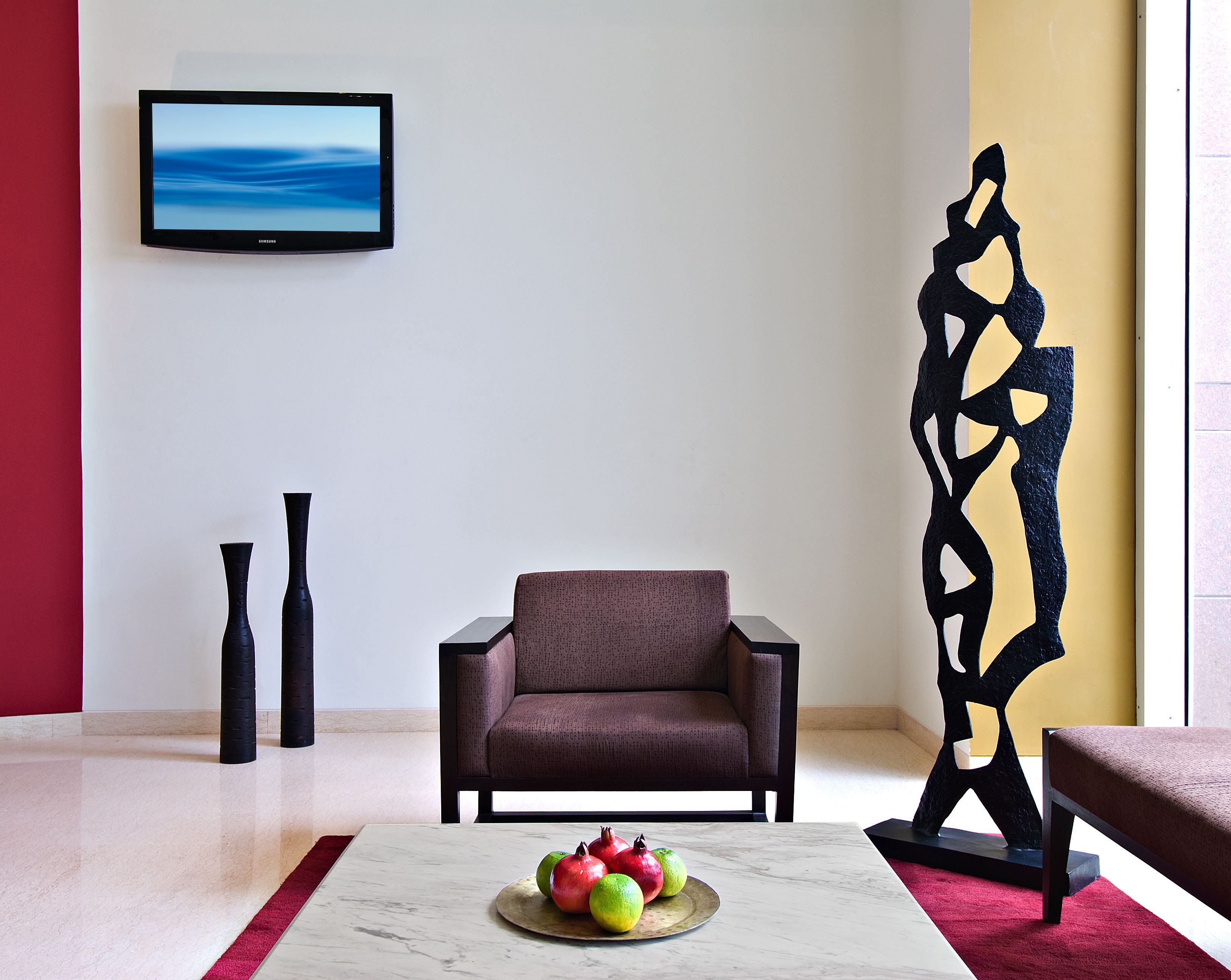 A modern living room with a brown armchair, a potted plant, and a fruit bowl on a marble table.