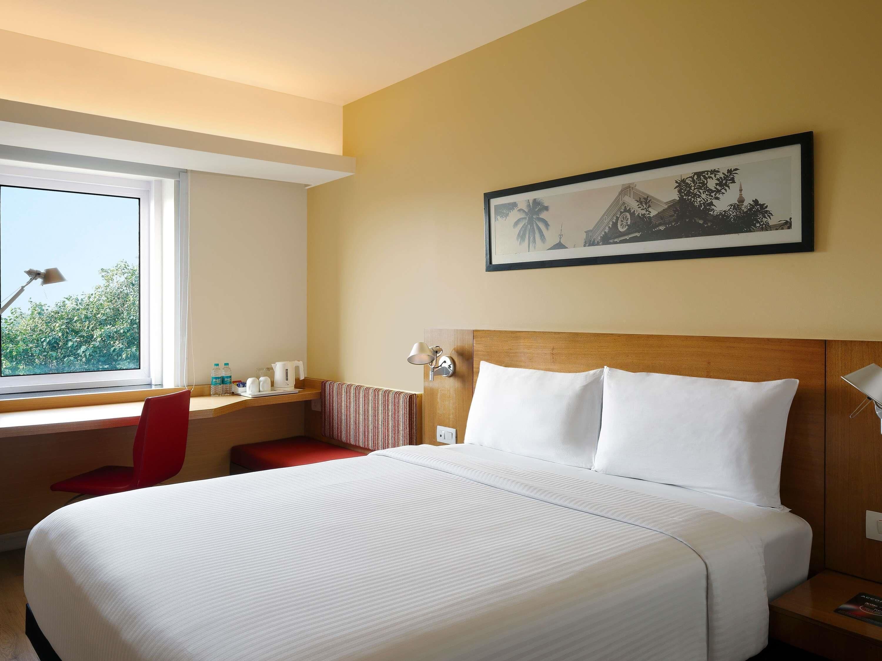 Habitación de hotel con una cama grande, un escritorio con silla, una ventana con vistas y un cuadro en la pared.