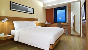 Habitación de hotel con cama, mesitas de noche, escritorio, silla, televisor y ventana.