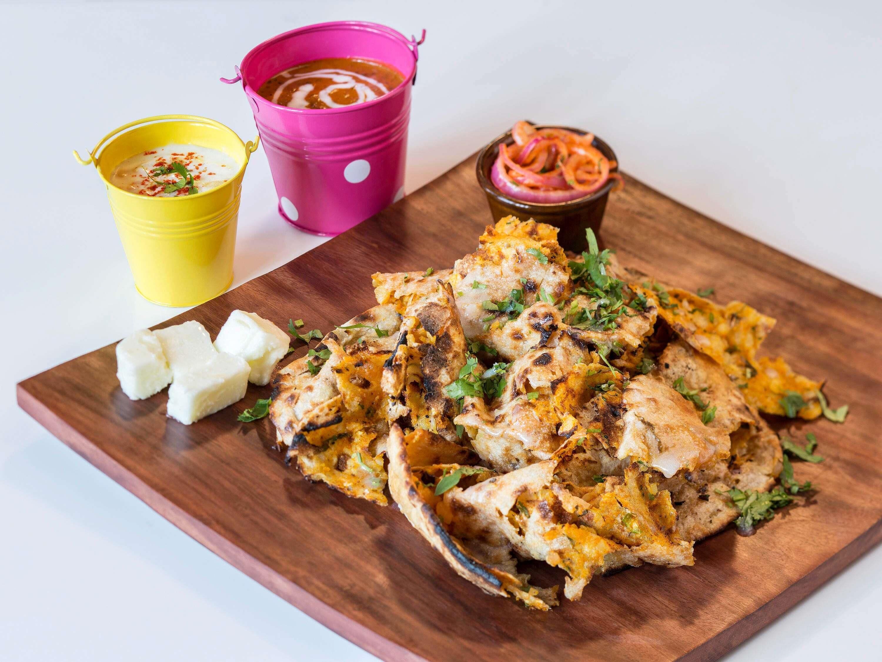Una tabla de madera con pollo a la parrilla, cubos de mantequilla y dos vasos de salsa de colores.
