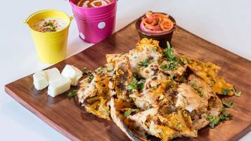 Una tabla de madera con pollo a la parrilla, cubos de mantequilla y dos vasos de salsa de colores.