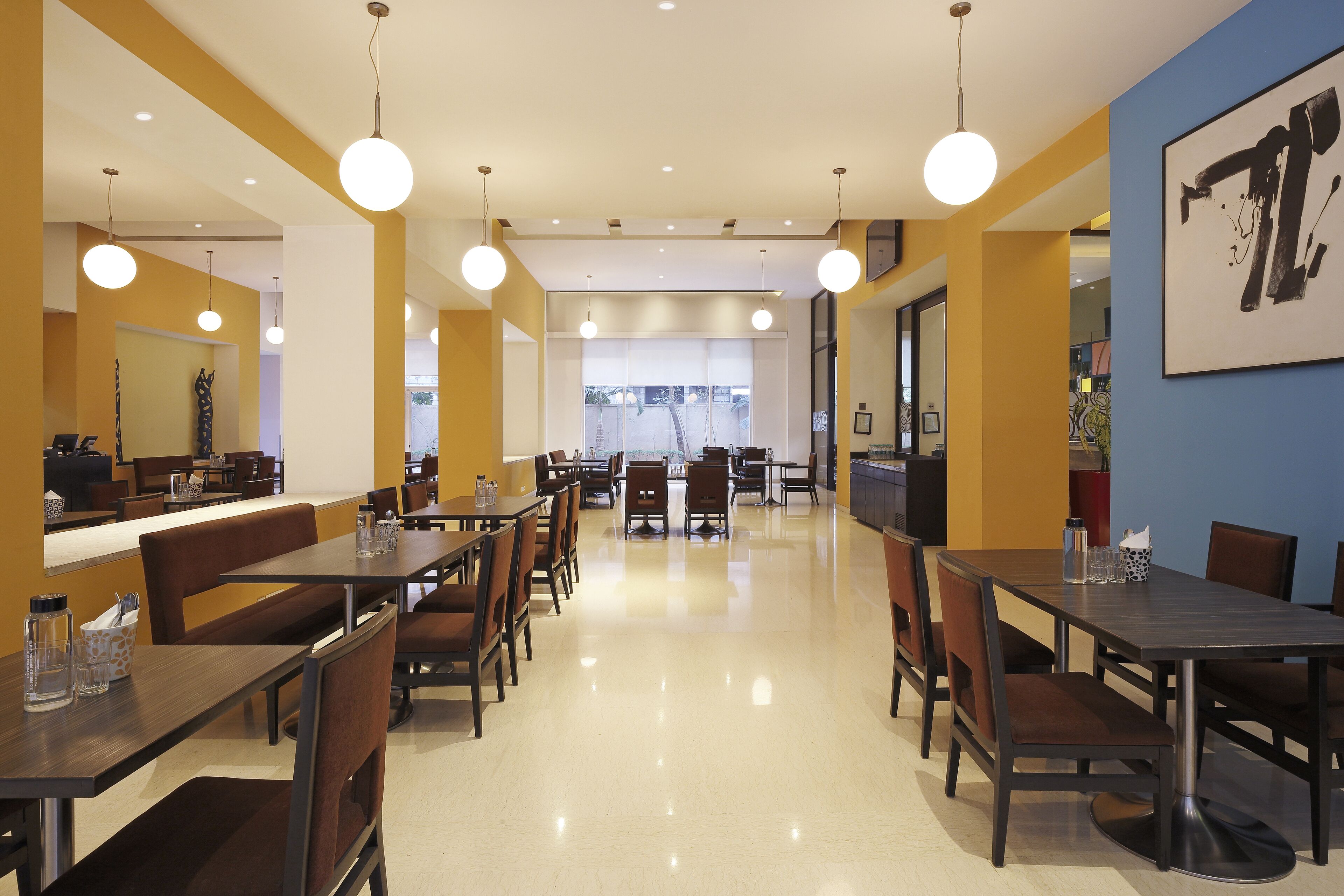 A modern dining area with multiple tables and chairs, a clean floor, and pendant lighting.