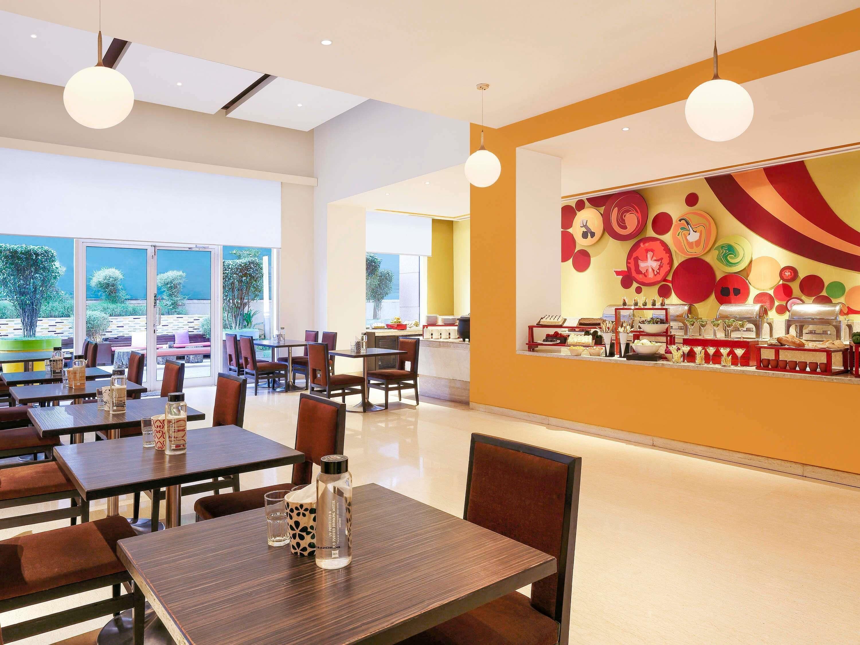 A modern dining area with tables and chairs, a buffet counter, and large windows offering a view of the outdoors.