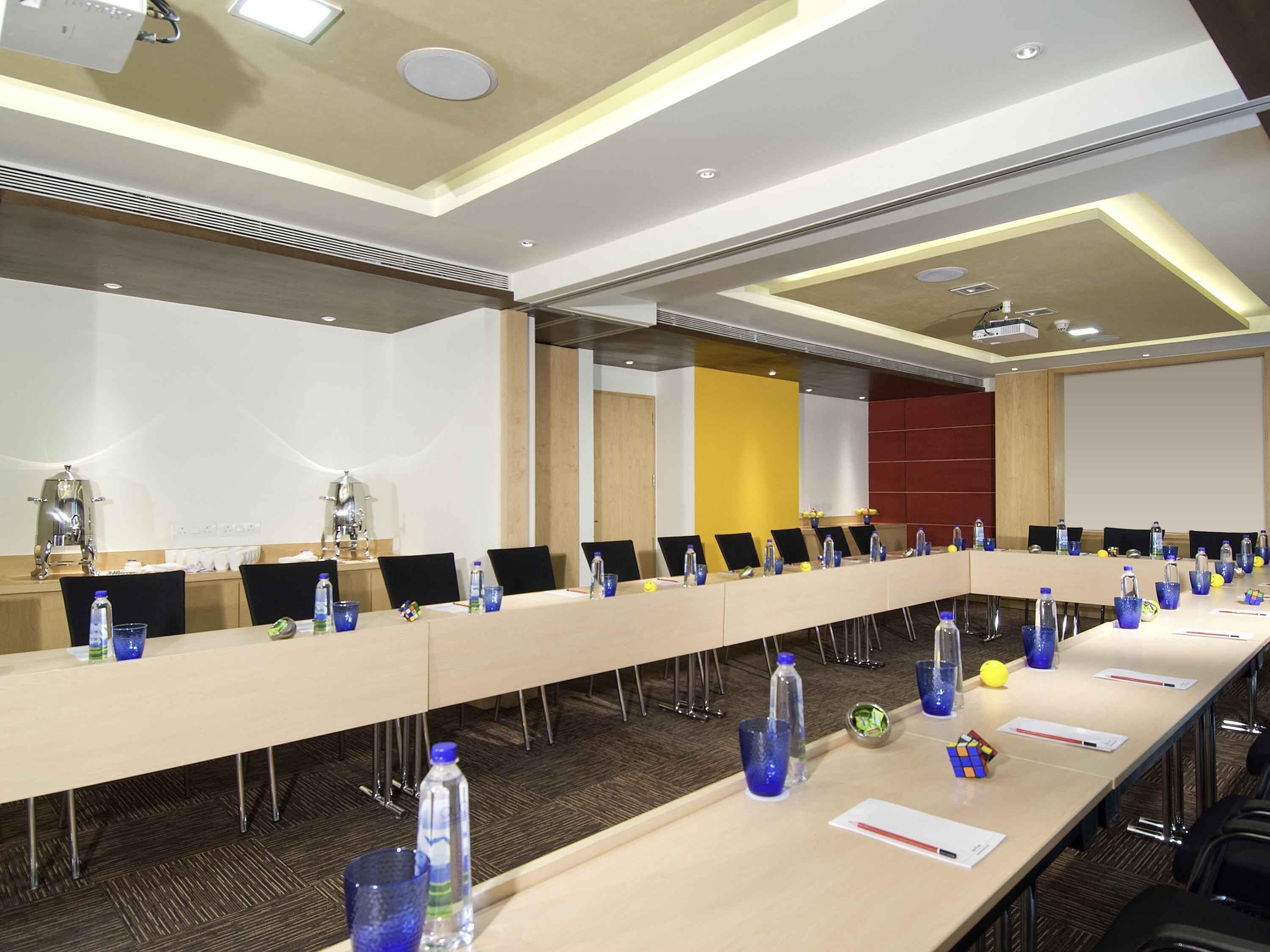 Una sala de conferencias con una larga mesa, sillas, botellas de agua y un proyector.