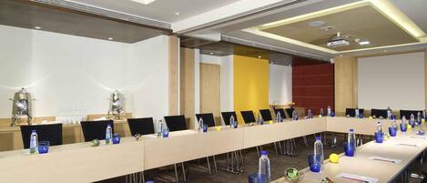 Una sala de conferencias con una larga mesa, sillas, botellas de agua y un proyector.