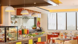 Un restaurante moderno con bufé, sillas de color naranja brillante y amplios ventanales.