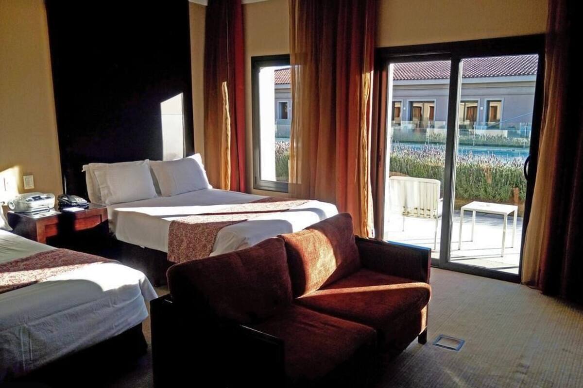 Ett hotellrum med två sängar, en soffa och en skjutdörr i glas som leder ut till en balkong.