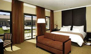 A hotel room with a large bed, a sofa, a desk, and a view of the outdoor pool area. - Hotel Casino Magic (Neuquén)