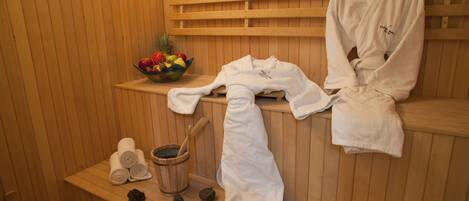 Un sauna con bancos de madera, toallas, un cubo de madera y un cuenco con fruta.